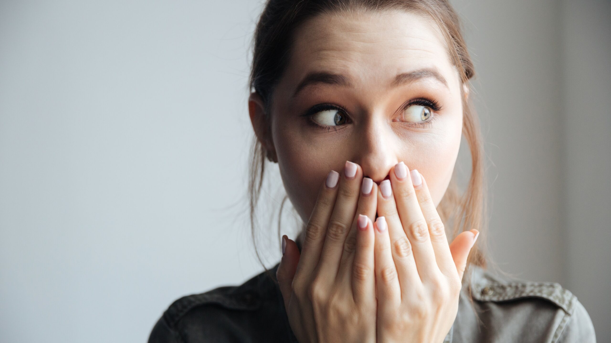 Young,Surprised,Woman,In,Shirt,Looking,Away.,Covering,Her,Mouth.